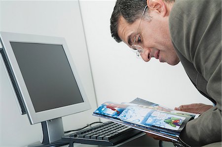 Mature man reading comic book at desk in office Stock Photo - Premium Royalty-Free, Code: 632-06354220