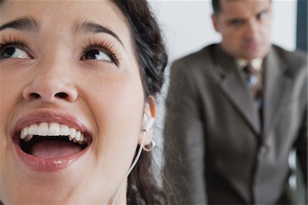 Woman listening to earphones and singing in office, angry boss in background Stock Photo - Premium Royalty-Free, Code: 632-06354423