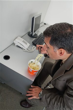 simsearch:632-07674665,k - Businessman eating ramen noodles at desk in office Stock Photo - Premium Royalty-Free, Code: 632-06353982