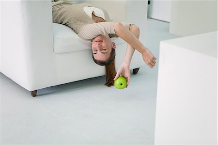 Woman lying upside down on sofa, holding apple Stock Photo - Premium Royalty-Free, Code: 632-06404175