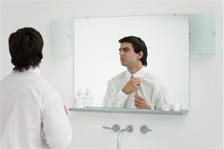 Man adjusting shirt collar in mirror Stock Photo - Premium Royalty-Free, Code: 632-06404410