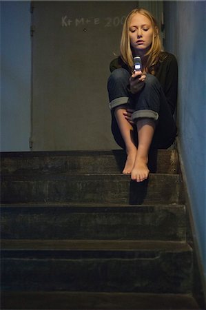 simsearch:632-06779169,k - Young woman sitting alone on stairs, looking at cell phone Photographie de stock - Premium Libres de Droits, Code: 632-06779240