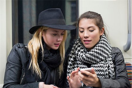 Young women sitting together on subway train, looking at smartphone Stock Photo - Premium Royalty-Free, Code: 632-07674520