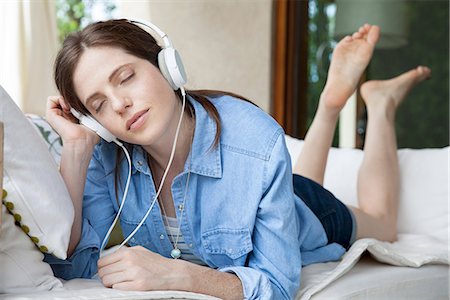 Young woma lying on stomach, listening to headphones with eyes closed Stock Photo - Premium Royalty-Free, Code: 632-08001810