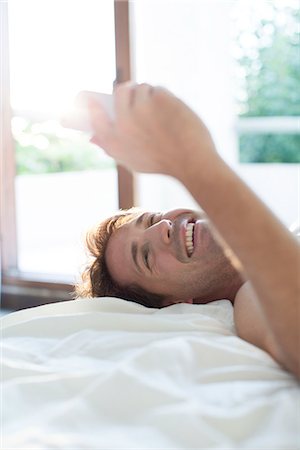 Man lying in bed using multimedia smartphone for instant messaging Stock Photo - Premium Royalty-Free, Code: 632-08130107