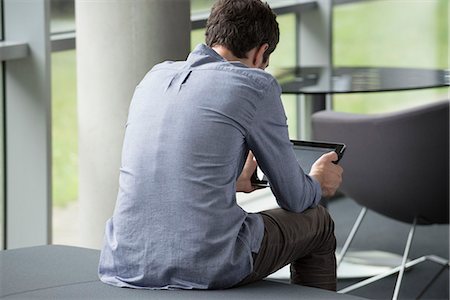 prelievo - Man sitting alone, looking at digital tablet, rear view Fotografie stock - Premium Royalty-Free, Codice: 632-08130299