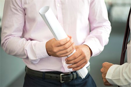 project development - Businessman holding rolled up blueprint, talking with colleague, cropped Photographie de stock - Premium Libres de Droits, Code: 632-08227858