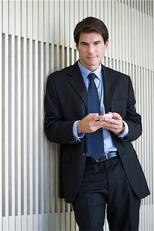 Businessman leaning against wall, using smartphone Stock Photo - Premium Royalty-Free, Code: 632-08698347