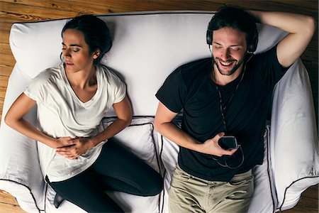 Woman holding stomach in pain while husband listens to mp3 player Foto de stock - Sin royalties Premium, Código: 632-08698603