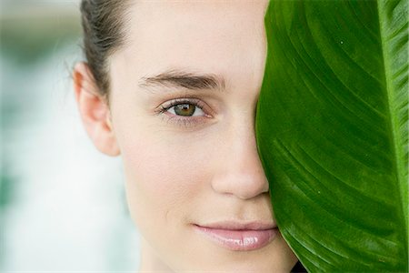 Young woman holding large leaf in front of her face and smiling Stock Photo - Premium Royalty-Free, Code: 632-09021415
