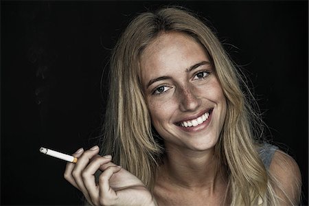 Young woman holding cigarette and smiling cheerfully, portrait Stock Photo - Premium Royalty-Free, Code: 632-09021568