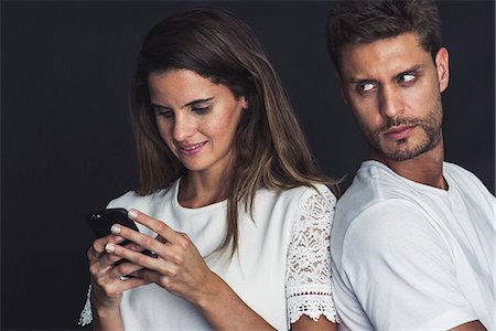 simsearch:632-09039785,k - Man glaring over his shoulder as girlfriend uses smartphone Stock Photo - Premium Royalty-Free, Code: 632-09039642