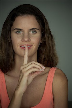 simsearch:632-06317597,k - Young woman smiling with finger held to lips Fotografie stock - Premium Royalty-Free, Codice: 632-09039956