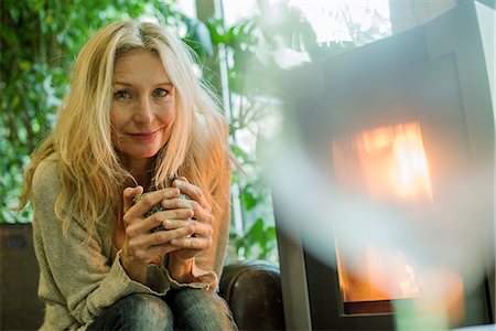 simsearch:632-09140316,k - Mature woman relaxing by fireplace with warm drink, portrait Stock Photo - Premium Royalty-Free, Code: 632-09140327