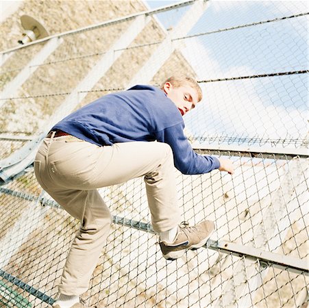 Young man climbing chainlink fence. Stock Photo - Premium Royalty-Free, Code: 632-01137632