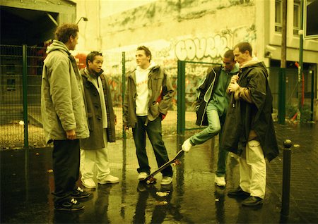 Young men hanging out together on street corner, wall with grafitti in background Stock Photo - Premium Royalty-Free, Code: 632-01137820