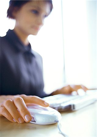 Businesswoman working on computer, blurred, focus on hand on mouse in foreground Stock Photo - Premium Royalty-Free, Code: 632-01147808