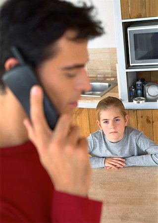 divorce children - Child looking at father on the phone in kitchen, blurred. Stock Photo - Premium Royalty-Free, Code: 632-01148285