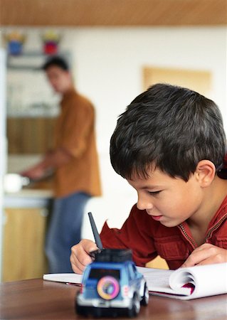 Son writing, father in background blurred. Stock Photo - Premium Royalty-Free, Code: 632-01148294