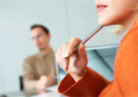 Businesswoman listening holding pen to her chin, man in background Stock Photo - Premium Royalty-Free, Code: 632-01148325