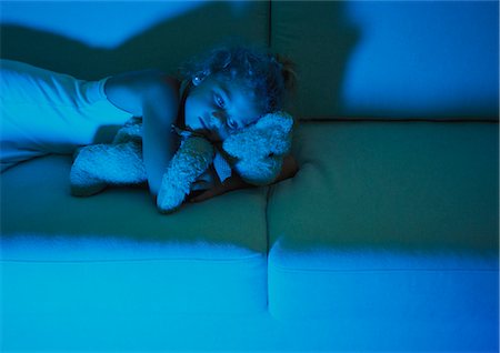 Petite fille allongée sur le canapé câlins avec ours en peluche, la lumière bleue de la télévision Photographie de stock - Premium Libres de Droits, Code: 632-01149214