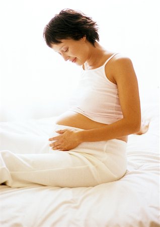 diffuse - Pregnant woman sitting on bed, looking at her stomach Stock Photo - Premium Royalty-Free, Code: 632-01140097