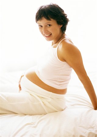 simsearch:632-01140071,k - Pregnant woman sitting on bed, smiling at camera, portrait Foto de stock - Sin royalties Premium, Código: 632-01140098