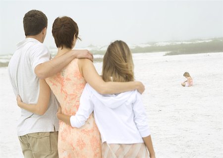 Parents and teenage daughter watching little girl play in sand in distance Stock Photo - Premium Royalty-Free, Code: 632-01155317