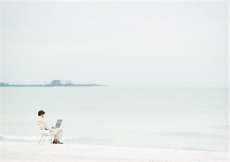 Businessman using laptop on beach, mid-distance Stock Photo - Premium Royalty-Free, Code: 632-01155545