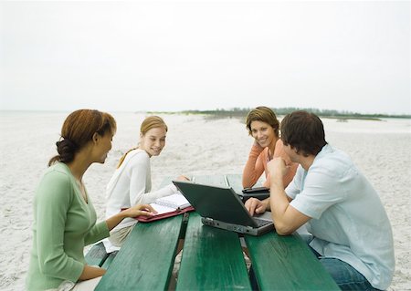 Four casually dressed adults sitting at picnic table on beach, with laptop and agendas Stock Photo - Premium Royalty-Free, Code: 632-01155540