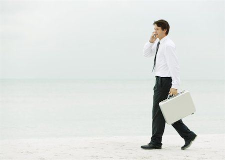 Businessman using cell phone and carrying briefcase on beach Stock Photo - Premium Royalty-Free, Code: 632-01155560