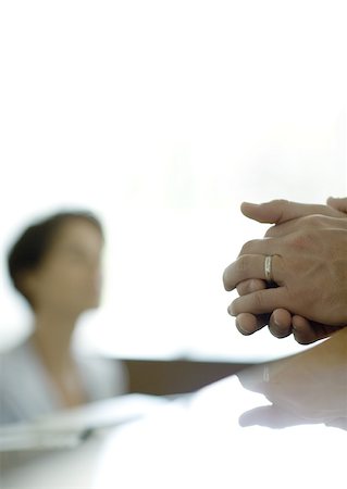 Man's clasped hands on reception desk, receptionist in background Stock Photo - Premium Royalty-Free, Code: 632-01155801