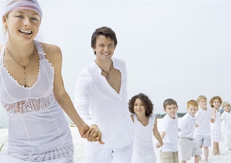 Bride and groom holding hands with line of children on beach Stock Photo - Premium Royalty-Free, Code: 632-01156011