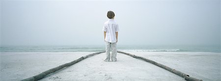 Boy standing in path on beach, facing horizon, rear view Stock Photo - Premium Royalty-Free, Code: 632-01156106