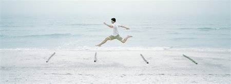 Man running and jumping over logs on beach Stock Photo - Premium Royalty-Free, Code: 632-01156119