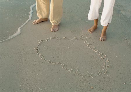 simsearch:633-05401372,k - Couple standing by heart drawn in sand, view of knee down Stock Photo - Premium Royalty-Free, Code: 632-01156252