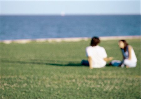 Young couple sitting together in grass by ocean, blurred Stock Photo - Premium Royalty-Free, Code: 632-01150040