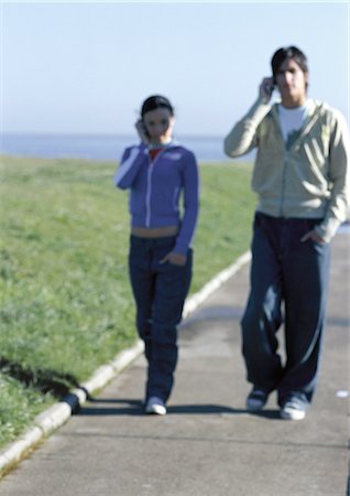 Young couple walking together, both talking on cell phones Stock Photo - Premium Royalty-Free, Code: 632-01150051