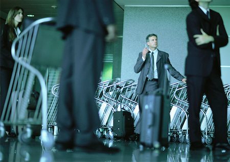 simsearch:695-03382908,k - A group of business people waiting, man by airport luggage carts using cell phone. Fotografie stock - Premium Royalty-Free, Codice: 632-01150102
