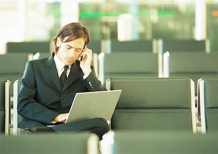 Businessman using cell phone and working on laptop in airport lounge Stock Photo - Premium Royalty-Free, Code: 632-01150114