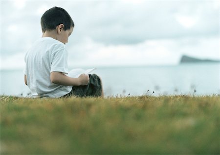 Boy reading on grass, sea in background, rear view Foto de stock - Sin royalties Premium, Código: 632-01150340