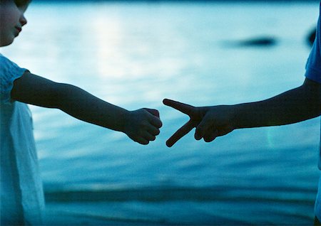 pedra papel tesoura - Children playing 'rock paper scissors', close-up, sea in background Foto de stock - Royalty Free Premium, Número: 632-01150384