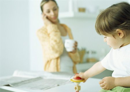 everyday family - Little girl playing with toy, woman holding mug and talking on phone in background Stock Photo - Premium Royalty-Free, Code: 632-01151509