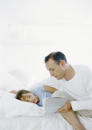 Homme assis sur le bord du lit en lisant un livre de fille couché dans son lit Photographie de stock - Premium Libres de Droits, Code: 632-01151549