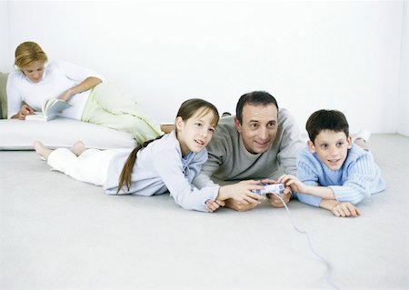 simsearch:633-02044233,k - Homme et garçon et fille couché sur le plancher de jeu vidéo, femme lisant en arrière-plan Photographie de stock - Premium Libres de Droits, Code: 632-01151541