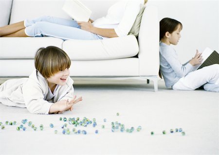 Boy playing marbles on floor, woman and girl reading in background Foto de stock - Sin royalties Premium, Código: 632-01151560