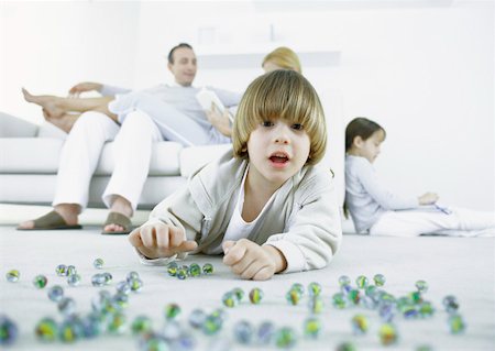 Boy lying on floor playing marbles, parents and sister sitting in background Foto de stock - Sin royalties Premium, Código: 632-01151561