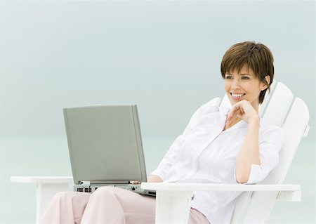 Woman sitting in deckchair using laptop, sea in background Stock Photo - Premium Royalty-Free, Code: 632-01160294