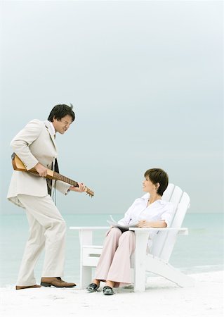 On beach, man in suit serenading woman sitting in deck chair Stock Photo - Premium Royalty-Free, Code: 632-01160296