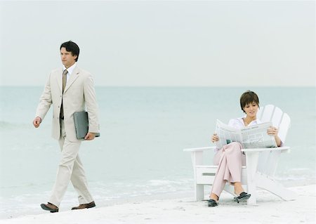 simsearch:632-01160695,k - On beach, businessman carrying laptop, walking by woman reading newspaper in chair Stock Photo - Premium Royalty-Free, Code: 632-01160297